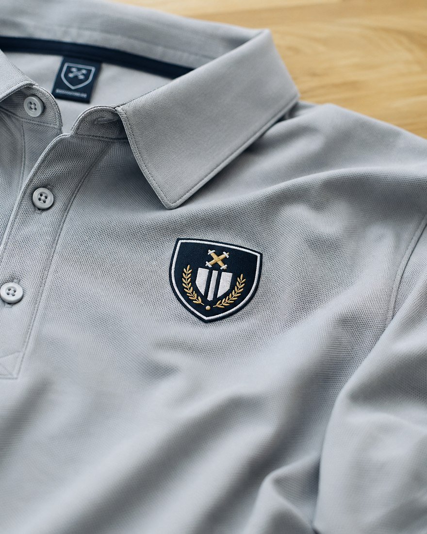 Close-up of an embroidered crest patch on a grey polo collar