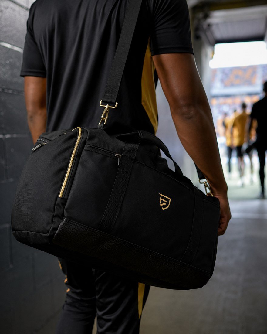 Athlete carrying a black and gold duffel bag through a stadium tunnel
