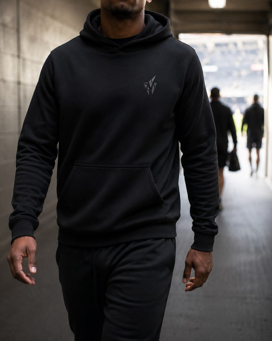 Athlete in a black hoodie and joggers walking through a stadium tunnel
